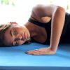 Woman performing relaxed Feldenkrais movements lying on a mat with eyes closed